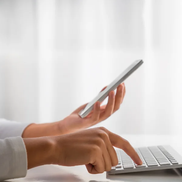 kobieta korzystająca jednocześnie z klawiatury komputera i ze smartfonu, stosując uwierzytelnianie dwuskładnikowe