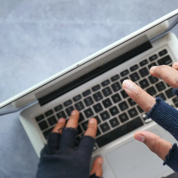 dłonie w rękawiczkach z wolnymi palcami dotykające klawiatury laptopa - zdjęcie symbolicznie obrazuje cyberprzestępstwa